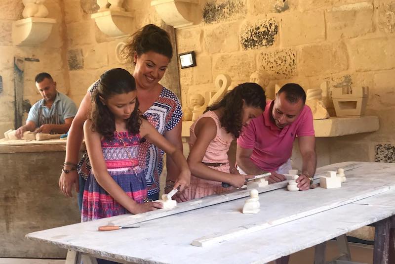 Famiglia impegnata al laboratorio dedicato alla tipica pietra calcarea maltese al Limestone Heritage Park and Garden